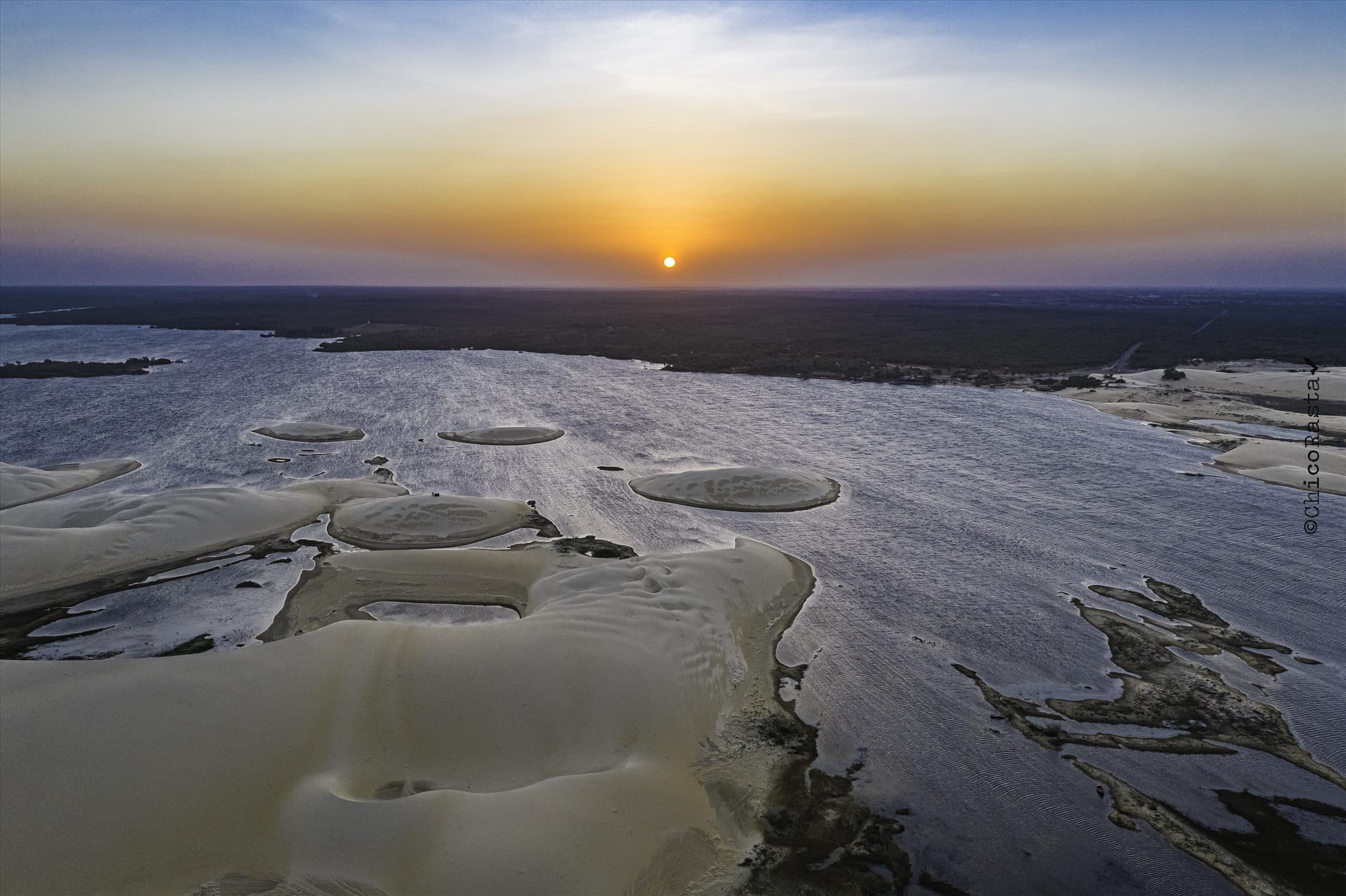 Pôr do sol visto sobre lagoa e dunas